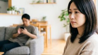 リビングでスマートフォンを見る夫と寂しそうな表情の妻
